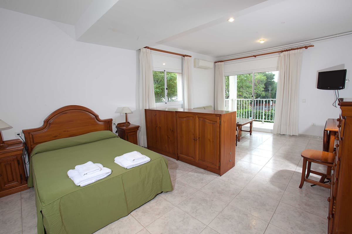 Ein Hotelzimmer mit Bett, Schreibtisch, Stuhl, Fernseher und einem Balkon mit Blick auf Grünflächen.