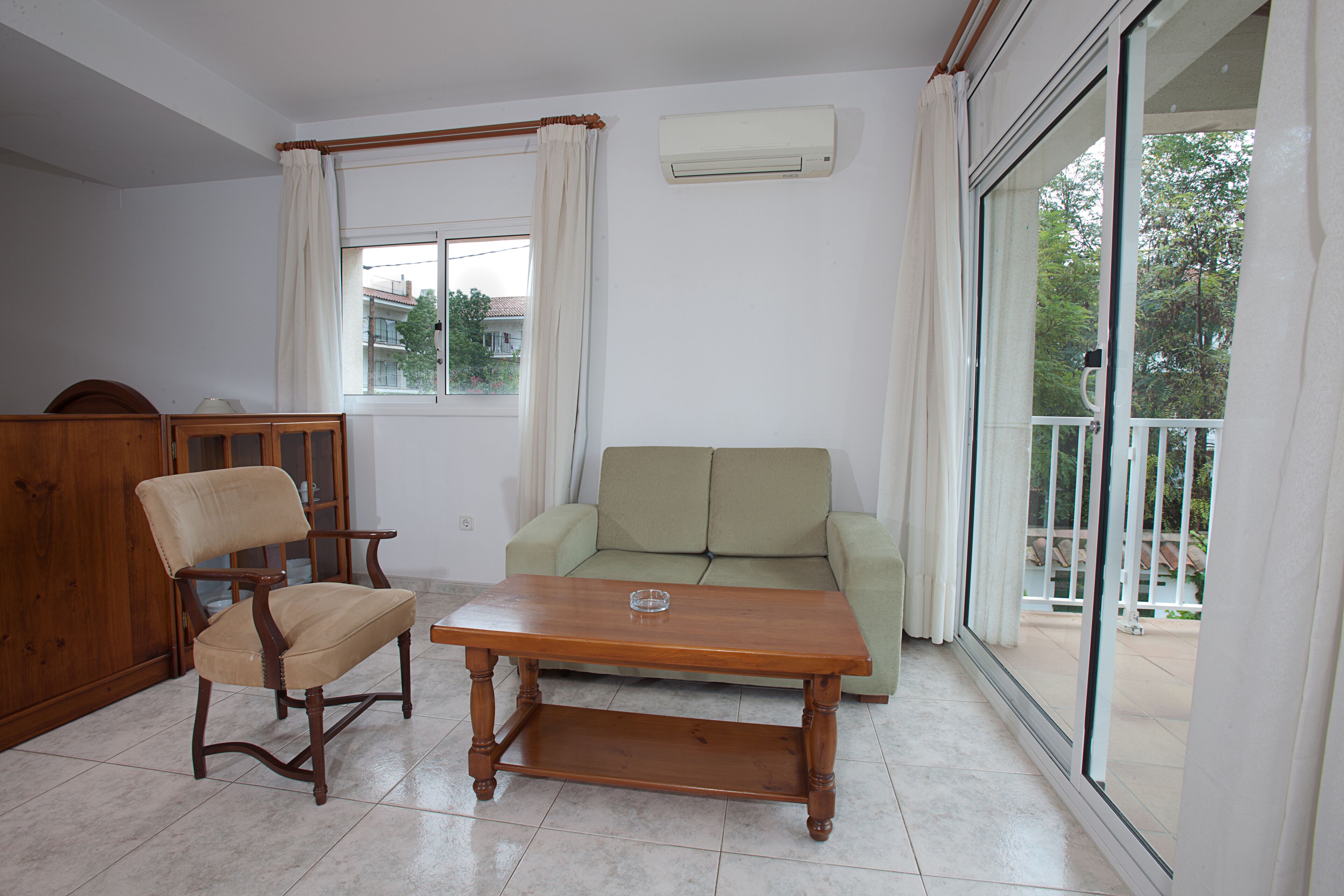 A living room with a wooden table, a green sofa, a wooden chair, and a glass door leading to an outdoor balcony.