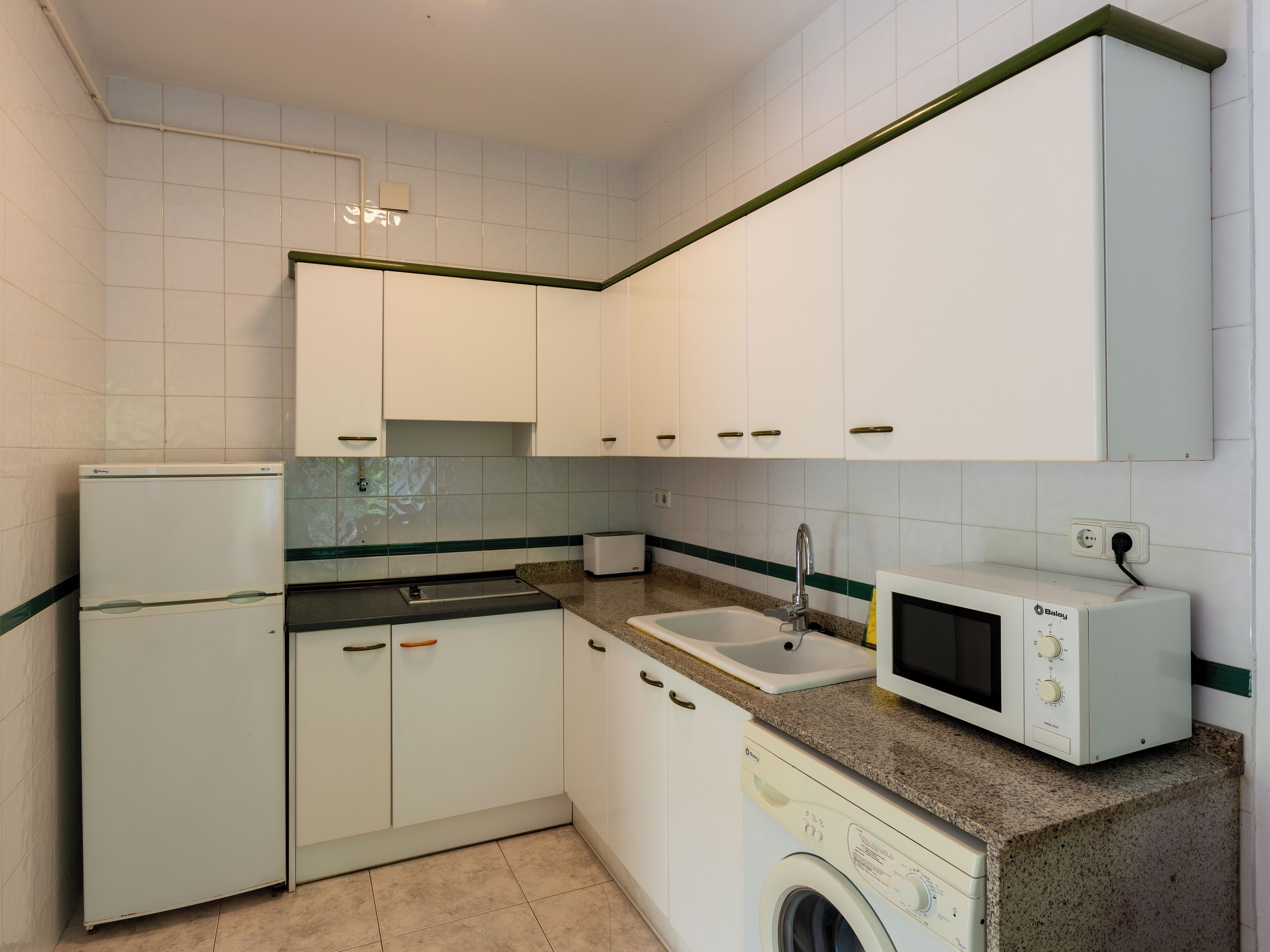 A compact kitchen with white cabinets, a washing machine, a microwave, and a sink.