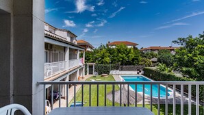 Ein Balkon mit Blick auf einen Swimmingpool, eine Rasenfläche und angrenzende Gebäude.
