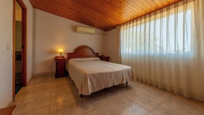 Ein Schlafzimmer mit Holzboden, einem Bett, einem Nachttisch, einer Lampe und einem Fenster mit Vorhängen.