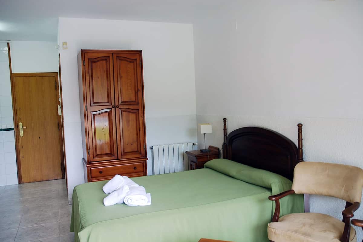 Ein Schlafzimmer mit einem Bett, einem Holzschrank, einem Sessel und einem Nachttisch.