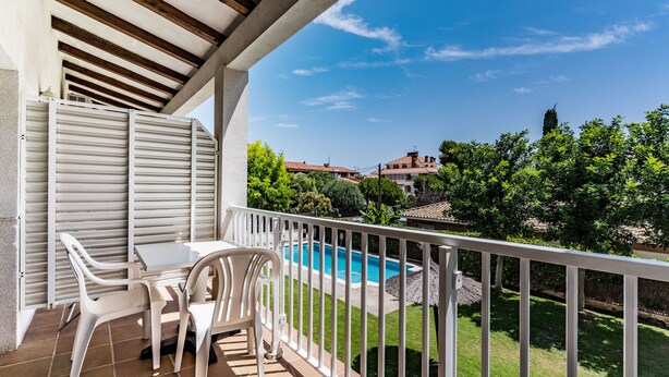Ein Balkon mit Blick auf einen Pool, weiße Stühle und ein gefliestes Podest.