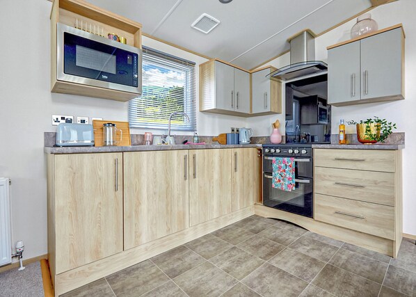 Una cocina moderna con armarios de madera, microondas integrado, estufa y pileta.