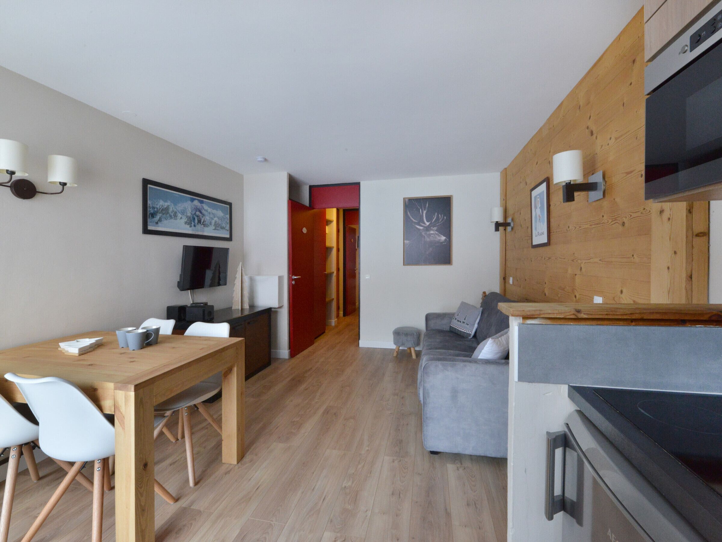 Un espacio de estar moderno con comedor, un sofá gris, una mesa de comedor de madera y una cocina con estufa.