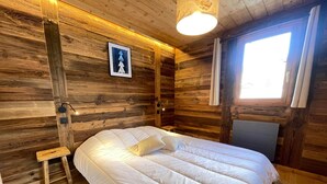Ein Zimmer in einer Holzhütte mit einem Bett, einem kleinen Nachttisch, einer Wandlampe und einem Fenster mit Vorhängen.