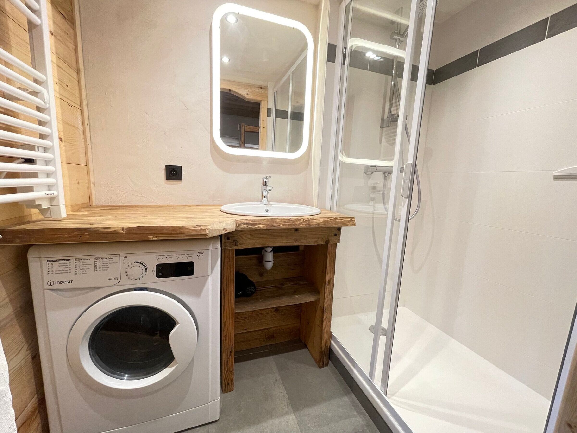 Un baño pequeño con lavadora, lavamanos y cabina de ducha de vidrio.