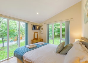 A bedroom with a large bed, a TV, and a view of a garden.