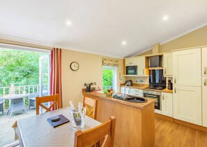 Une cuisine avec un îlot central en bois, une table à manger avec des chaises, une horloge au mur et une vue sur la verdure à l’extérieur.