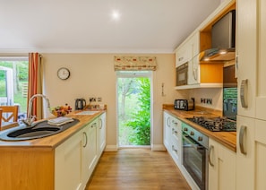 Cozinha moderna com bancada de madeira, eletrodomésticos de aço inoxidável e vista para o verde lá fora.