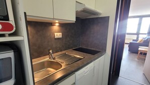Ett kompakt kök med en diskho i rostfritt stål, vita skåp och en inbyggd diskmaskin.
