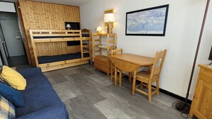 Ett rum med en våningssäng, ett matbord med stolar, en soffa, en lampa och en inramad tavla på väggen.