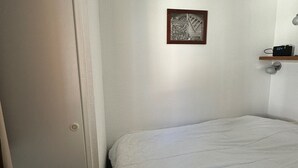 Un dormitorio con cama, una puerta, un estante con cámara fijada a la pared y un cuadro enmarcado.