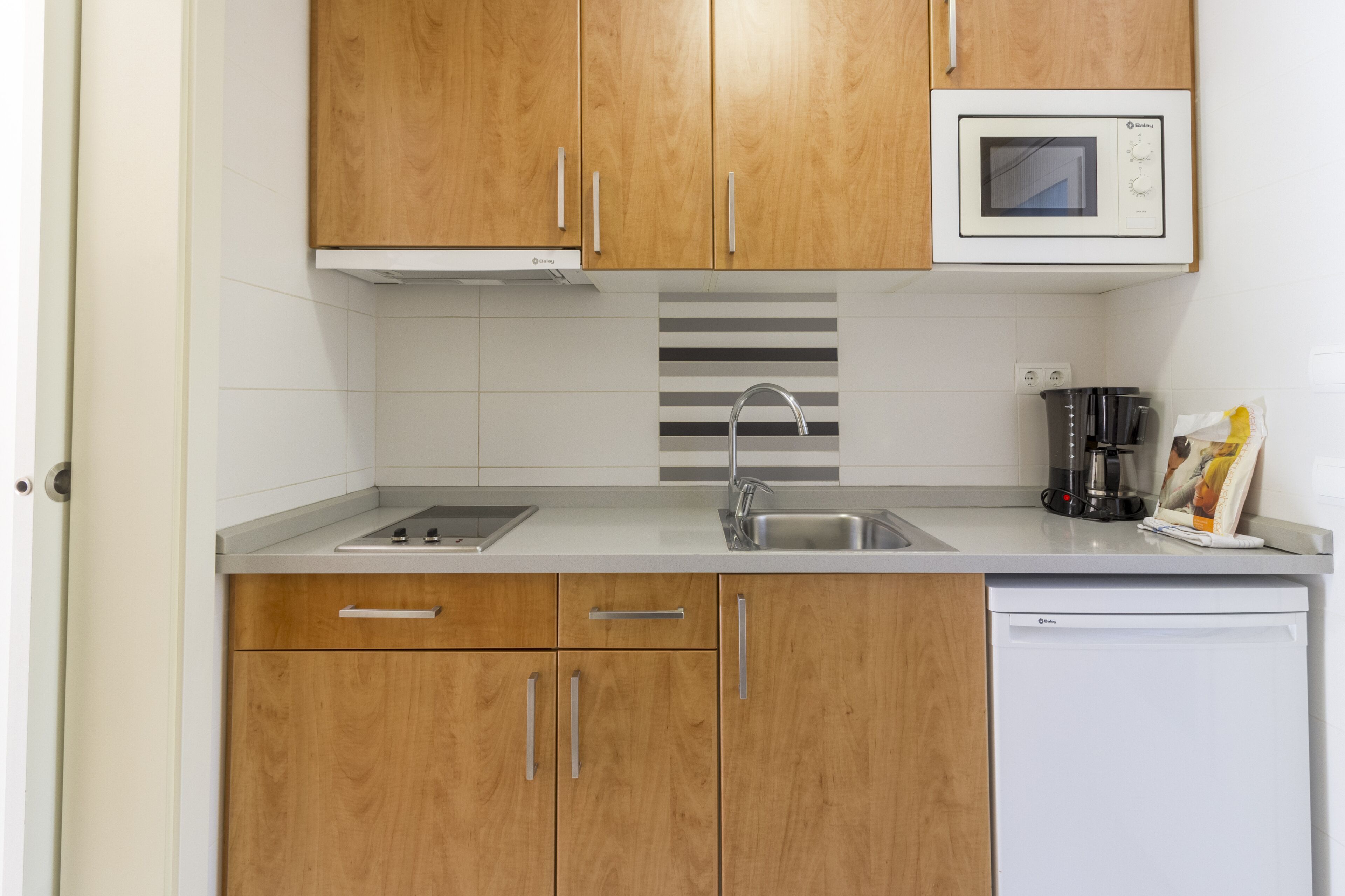 A modern kitchen with wooden cabinets, a stainless steel sink, a microwave, and a coffee maker.