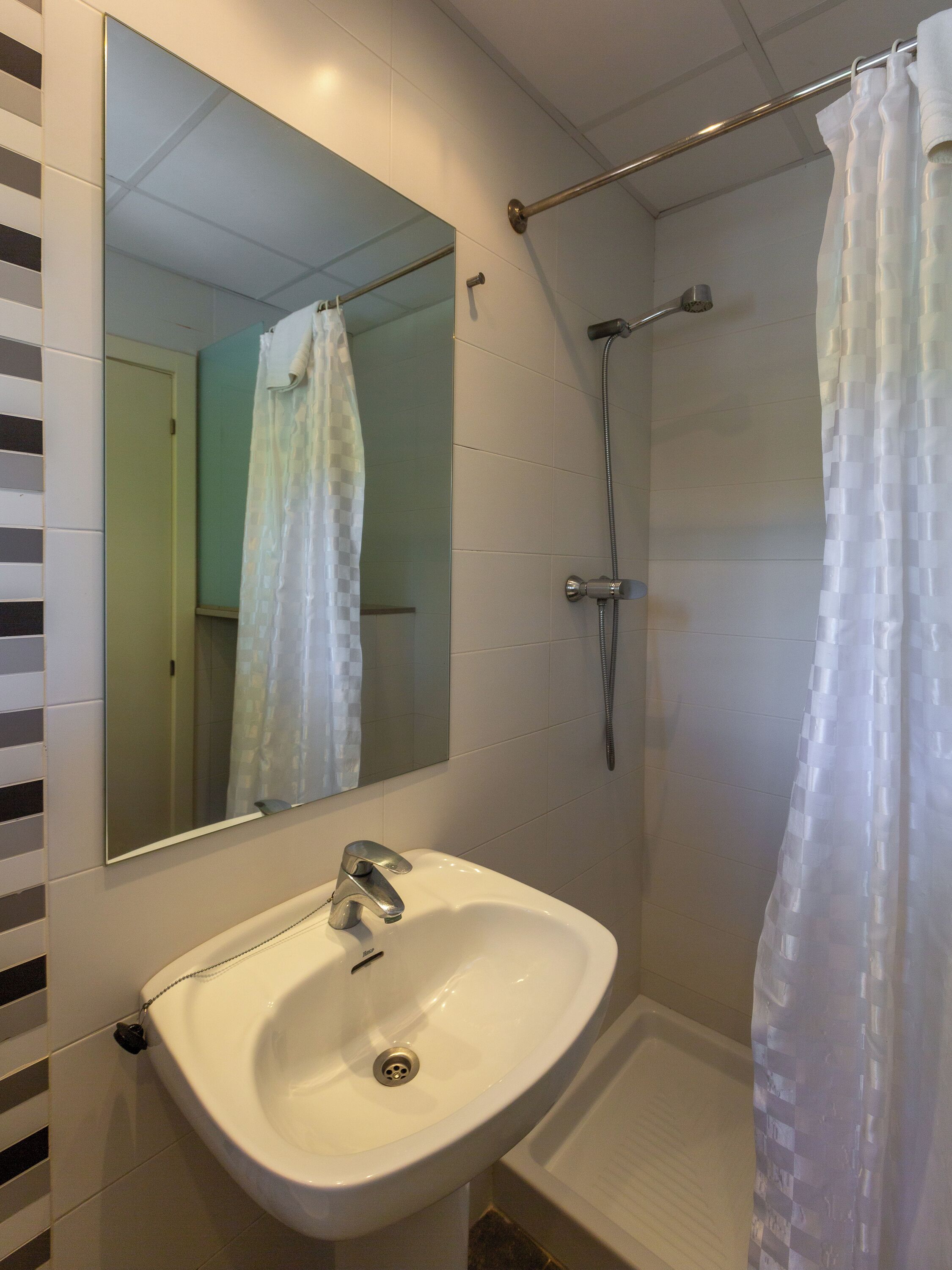 A bathroom with a white sink, a mirror, a shower with a curtain, and tiled walls.