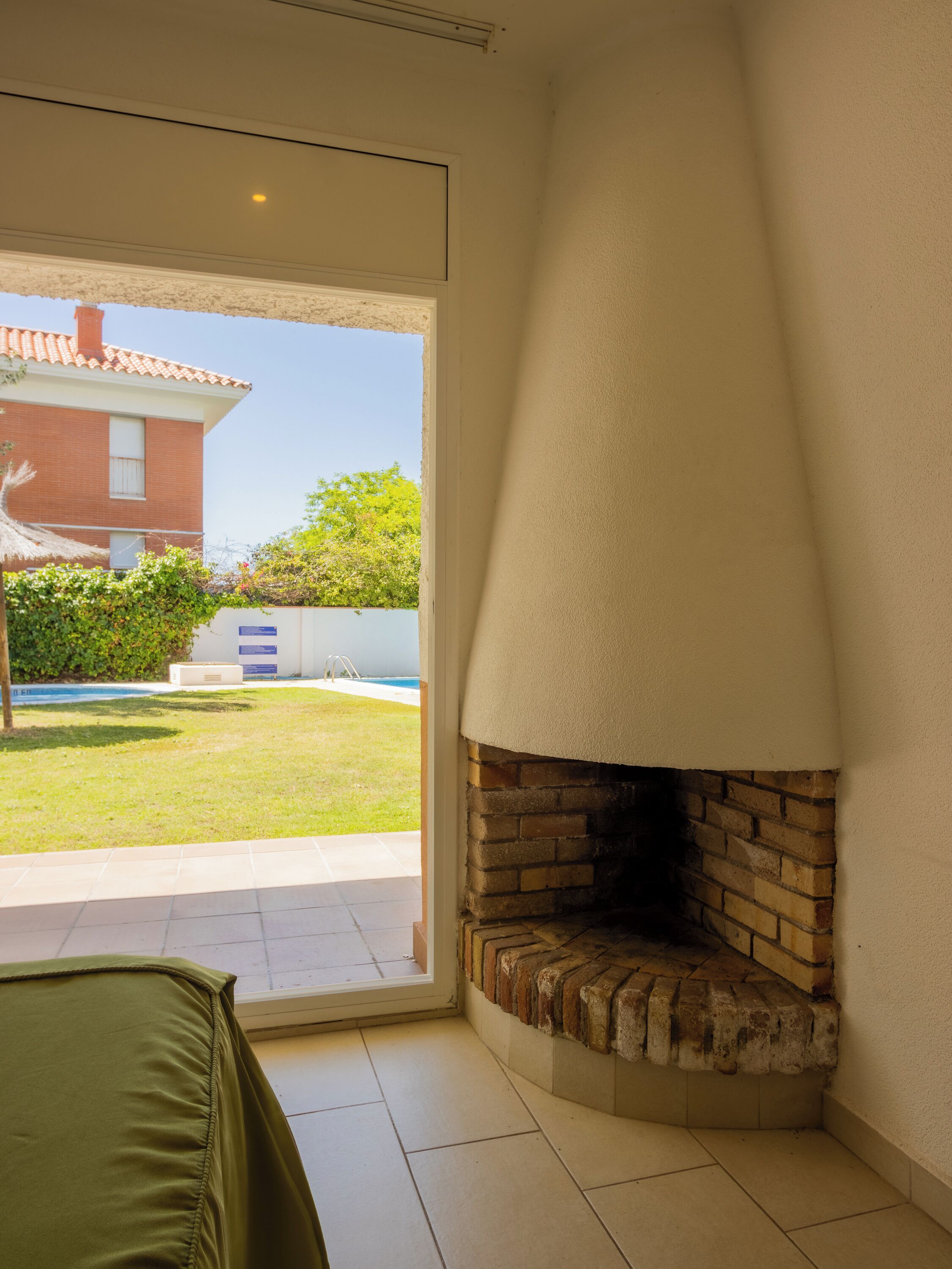 Una habitación con chimenea de ladrillo, puerta corrediza de vidrio que da a un patio con piscina y un sofá verde.