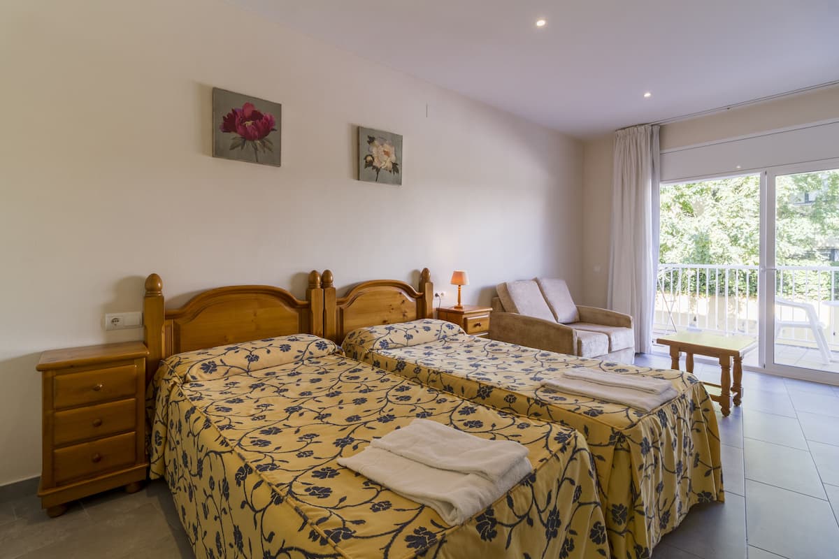 Habitación doble con dos camas, una mesita de noche, una silla, una mesa y un balcón con vistas.