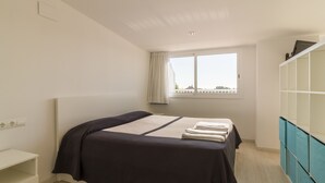 A bedroom with a bed, a window with curtains, a white nightstand, and a built-in cabinet. - SUNWAY SAN JORGE (Sitges)