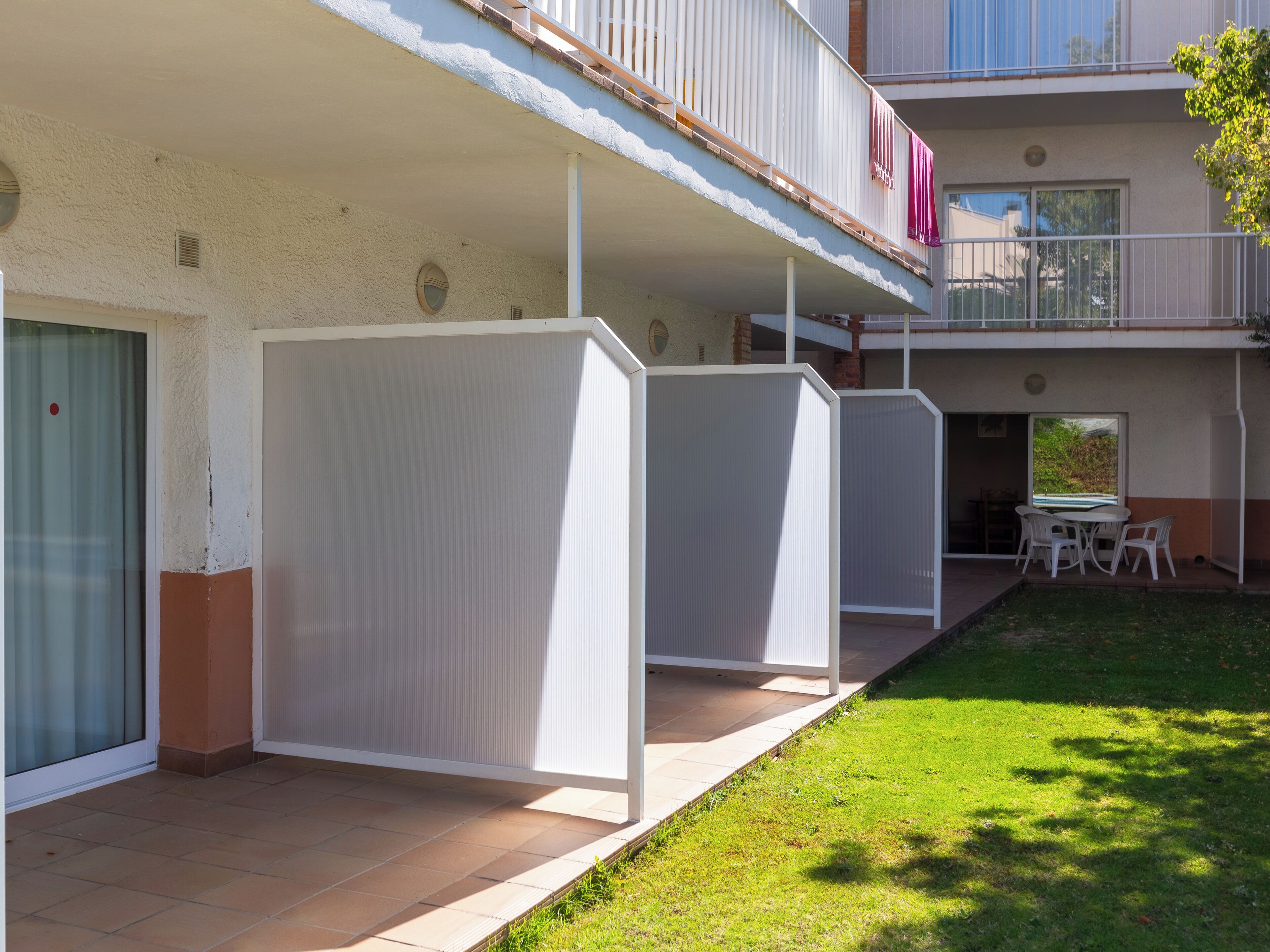 A residential building with a covered patio area, a small outdoor seating area, and a view of the surrounding greenery.