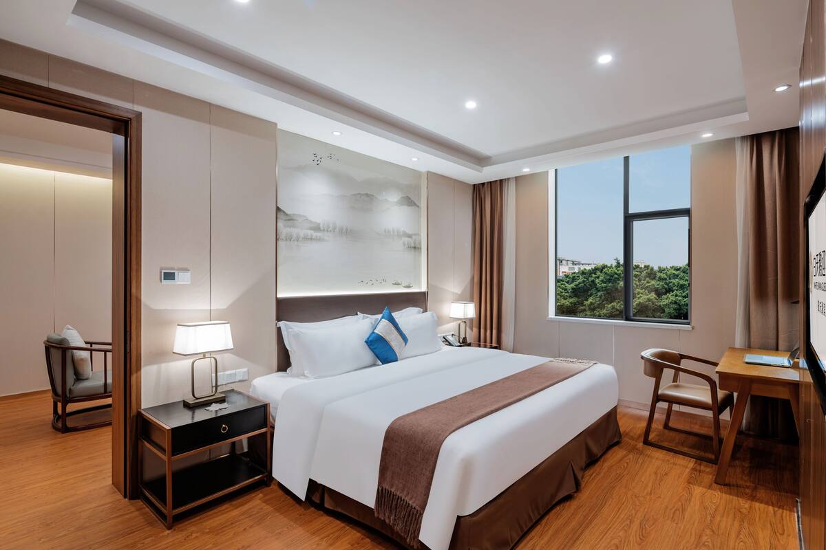 Ein Hotelzimmer mit einem großen Bett, Nachttischen, einem Schreibtisch und Blick auf Grünflächen.