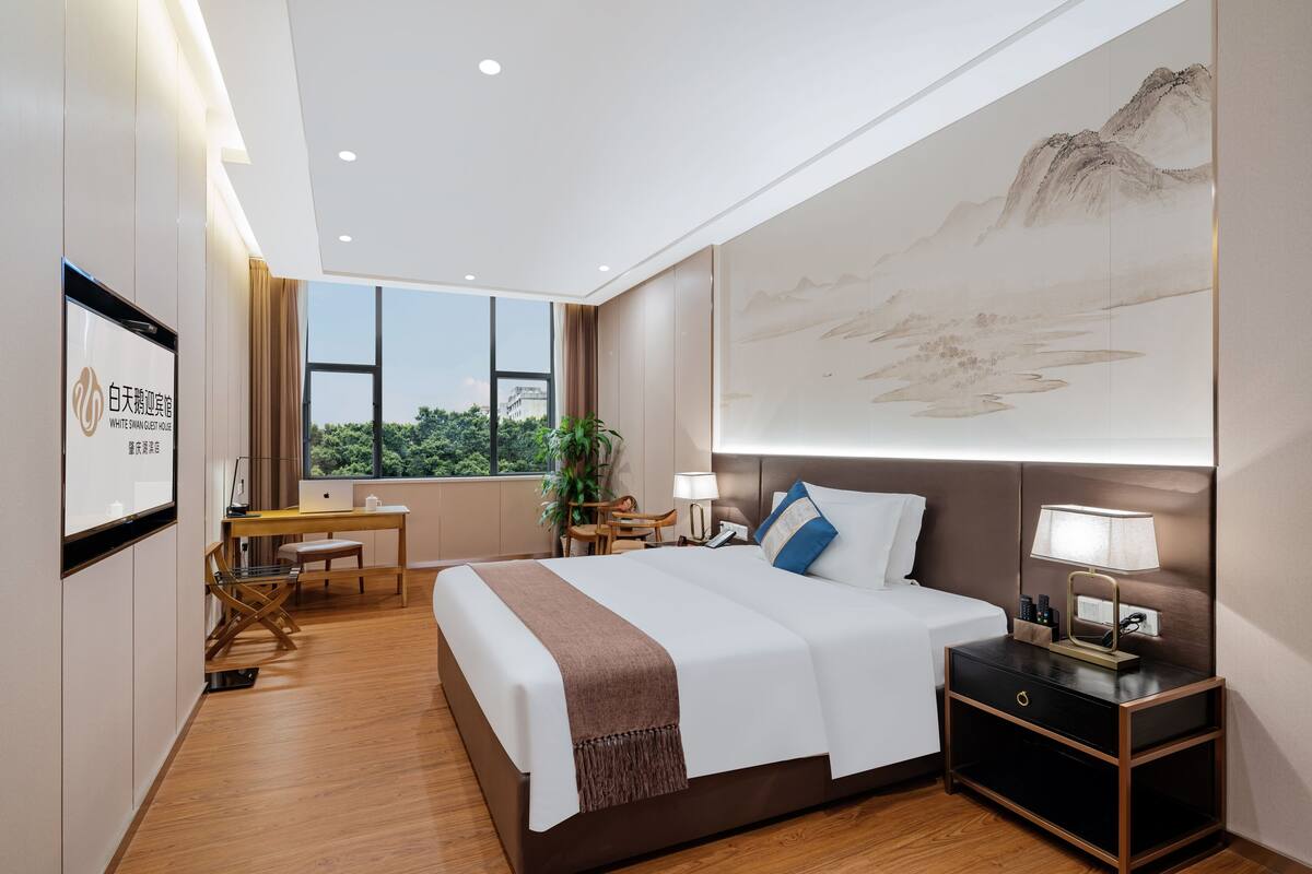 Une chambre d’hôtel dotée d’un grand lit, de tables de chevet, d’un bureau et d’une grande fenêtre donnant sur l’extérieur.