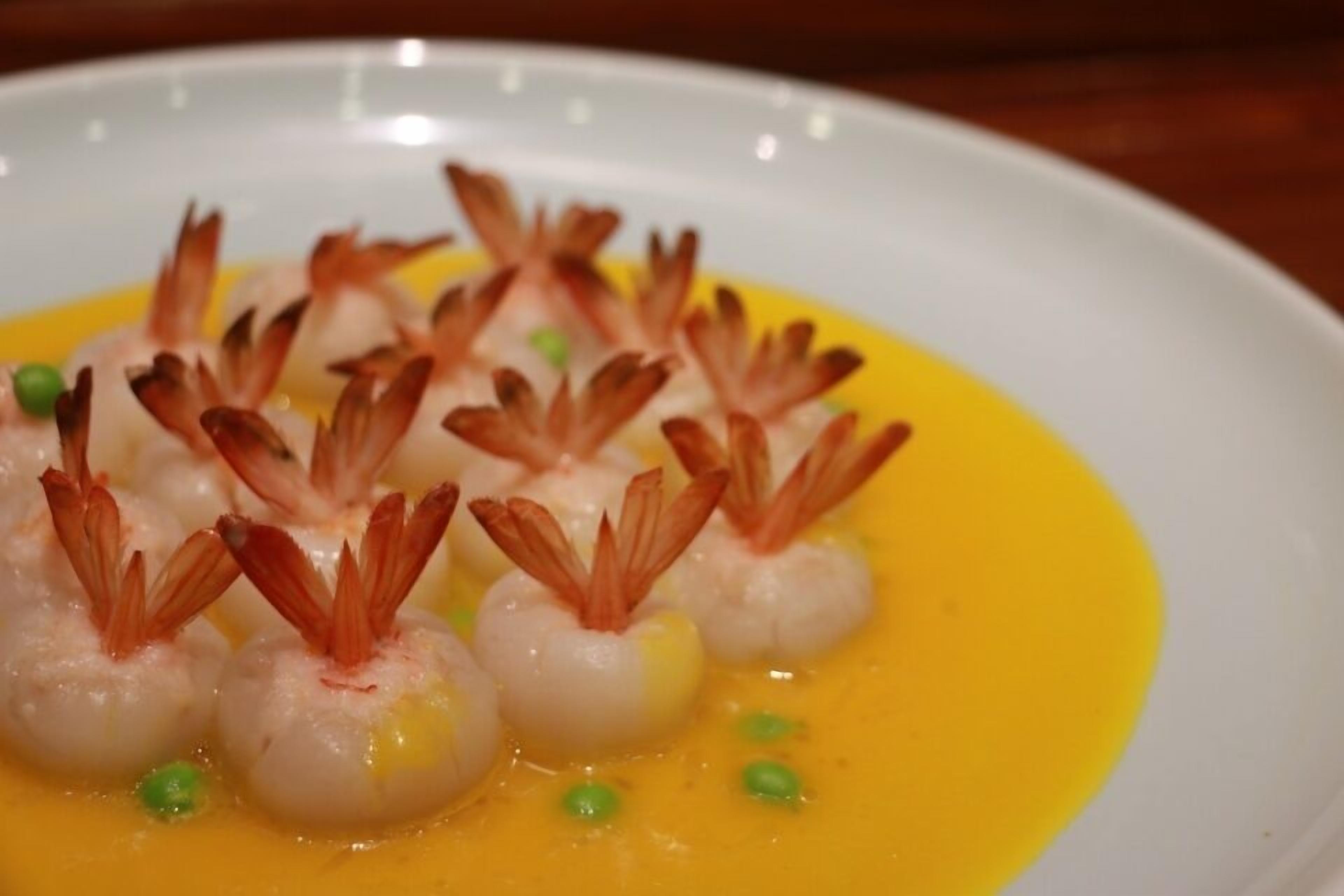 A plate of shrimp with a yellow sauce and green garnish.