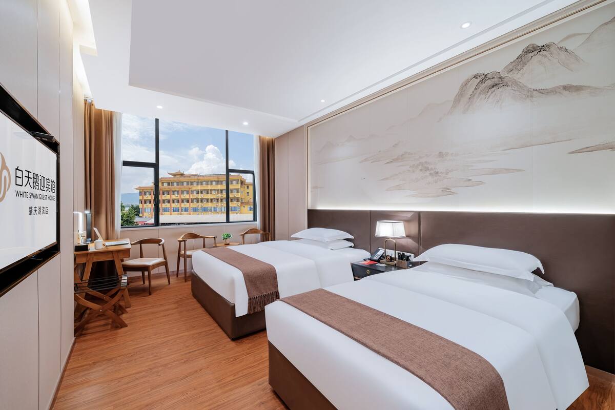 Une chambre d’hôtel avec deux lits, un bureau, des chaises et une grande fenêtre donnant sur un immeuble.