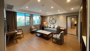 A modern hotel room with a sofa, chairs, a coffee table, a desk, and a large window offering a city view. - White Swan Guest House (Zhaoqing)