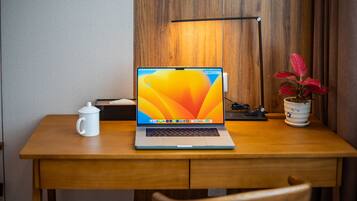 Un escritorio de madera con una computadora portátil, una taza blanca, una lámpara y una planta en maceta.