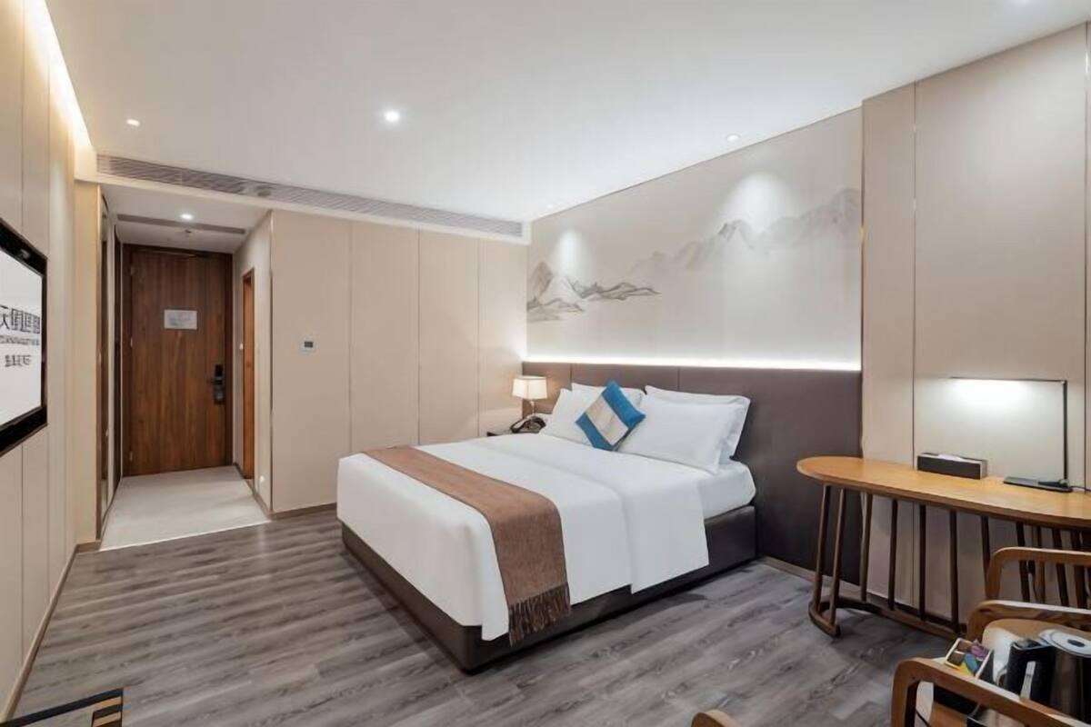 Une chambre d’hôtel moderne équipée d’un lit, d’une table de chevet, d’une lampe et d’un petit bureau avec une chaise.