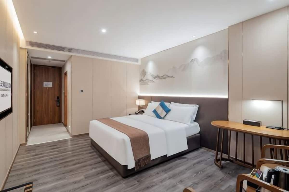 Quarto de hotel moderno com cama, mesa de cabeceira, abajur e uma pequena escrivaninha com cadeira.