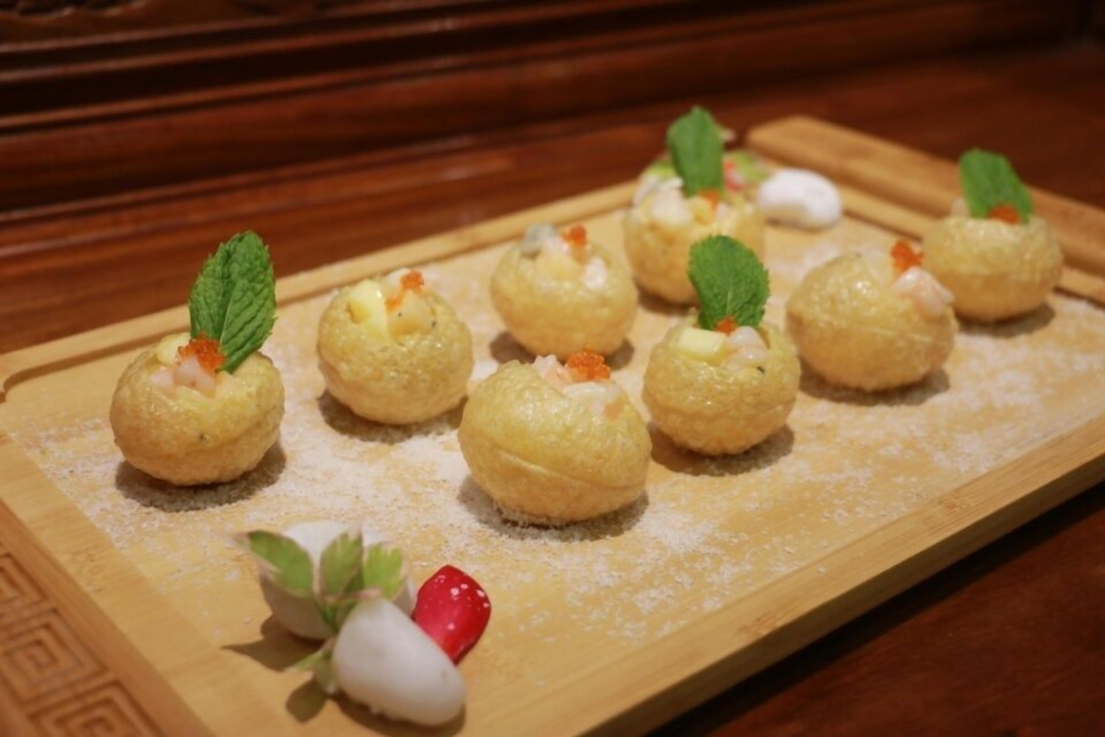 A wooden serving board with small, round pastries topped with mint leaves and a strawberry.