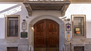 A large wooden double door with a stone archway above, flanked by two windows with metal bars. - Santa Marta Suites (Milan)