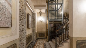 A hallway with a stone column, a staircase with ornate metal railings, and a tiled floor. - Santa Marta Suites (Milan)