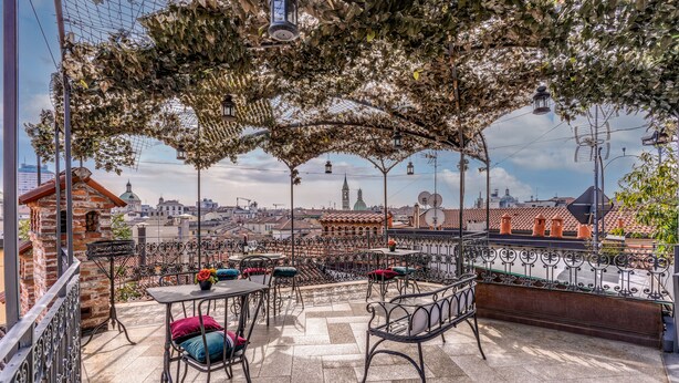 An outdoor terrace with tables and chairs, a view of the cityscape, and a pergola with hanging lanterns. - Santa Marta Suites (Milan)