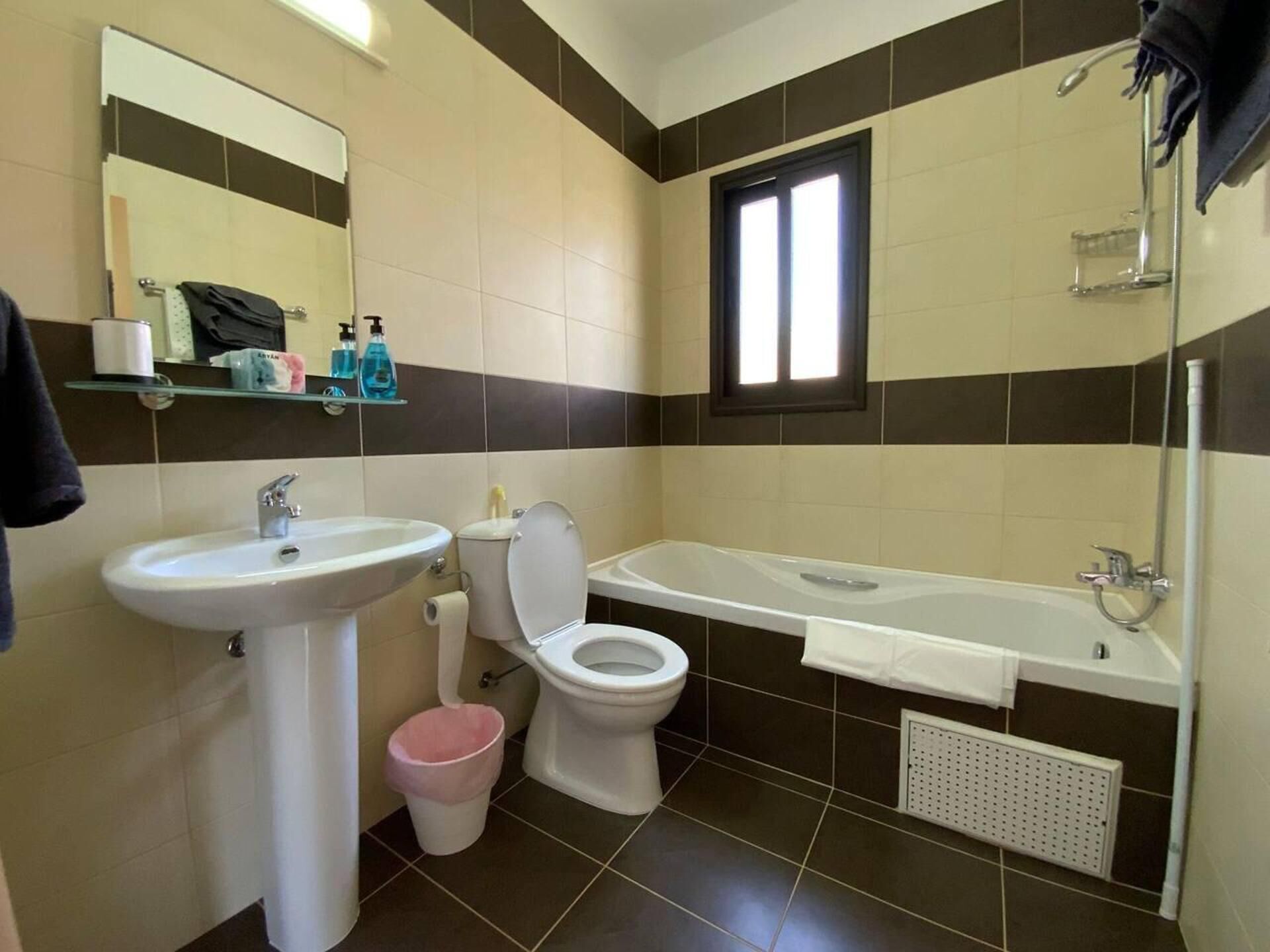 A bathroom with a sink, toilet, and bathtub. There is a window above the bathtub and a mirror above the sink.