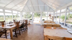 A spacious conservatory with large windows, wooden furniture, and a view of the outdoors. - Far Coley Farm &amp; Log Cabin (Stafford)
