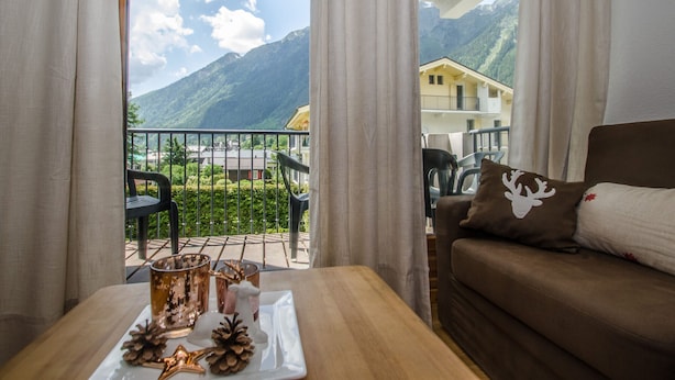 Et værelse med udsigt til bjerge, en balkon med udendørs møbler og et bord med pynt.
