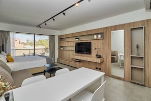 A modern hotel room with a bed, a desk, a TV, and a balcony with a city view.
