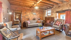 A cozy living room with a brick wall, wooden beams, and a variety of seating including a sofa, armchairs, and a coffee table with books and flowers. - The Old Cartshed - AWARD WINNING Eco conversion ,sleeps 10, Peak District views SC (Leek)