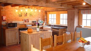 A rustic kitchen with wooden cabinetry, a central island, and a dining table with chairs. - The Old Cartshed - AWARD WINNING Eco conversion ,sleeps 10, Peak District views SC (Leek)