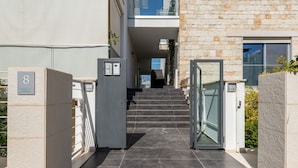 Une entrée moderne, avec un escalier menant à un deuxième étage, un espace délimité par une grille et une porte dotée d’un panneau en verre.