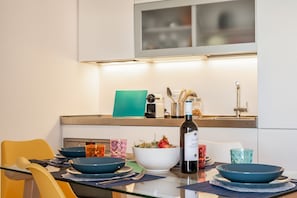 Une cuisine moderne avec une table à manger dressée pour deux personnes, une bouteille de vin et divers ustensiles de cuisine.