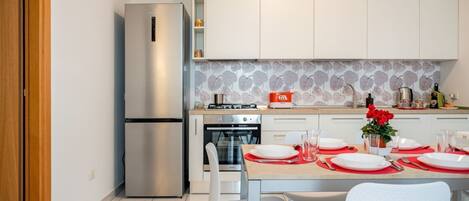 A modern kitchen with stainless steel appliances, white cabinetry, and a tiled backsplash.