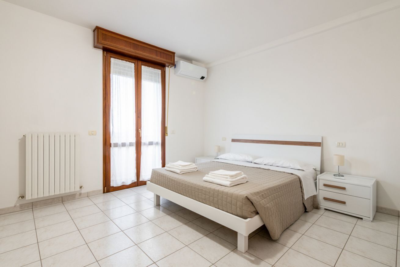 Un dormitorio con cama, mesita de noche, lámpara, radiador y puerta corrediza de vidrio.