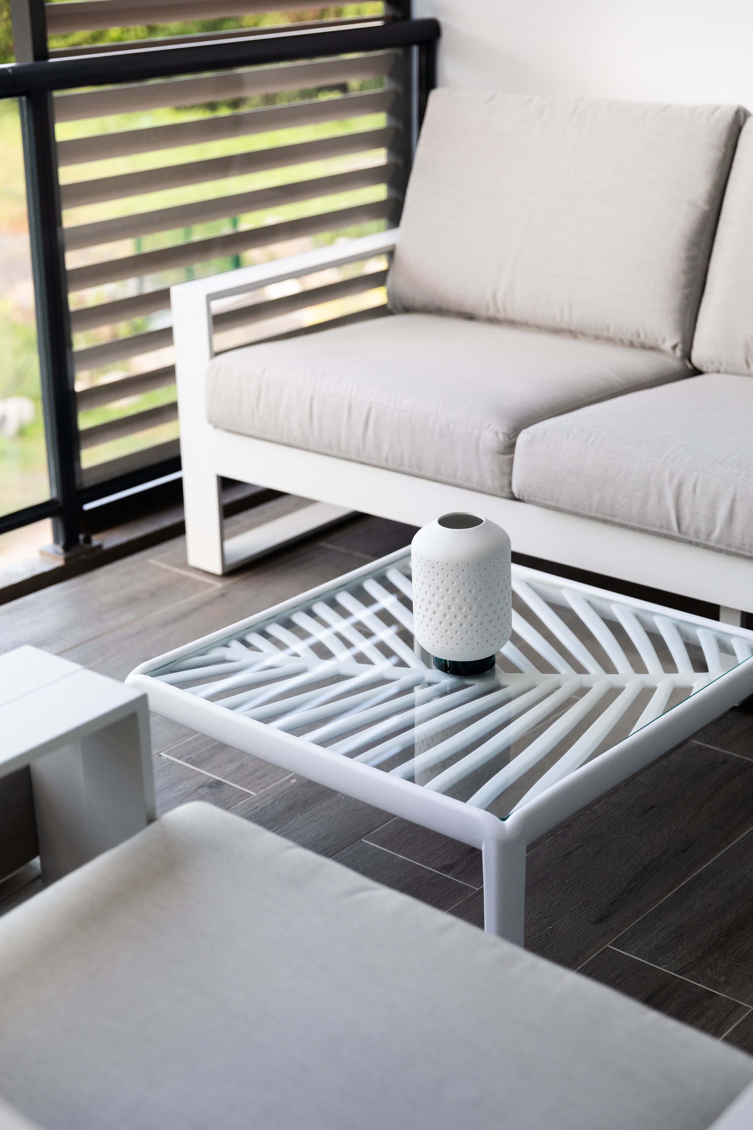 A modern living room with a white sofa, a glass coffee table with a geometric pattern, and a white vase.