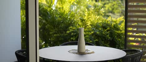 A round table with a white vase, surrounded by black chairs, in a room with large windows overlooking lush greenery.