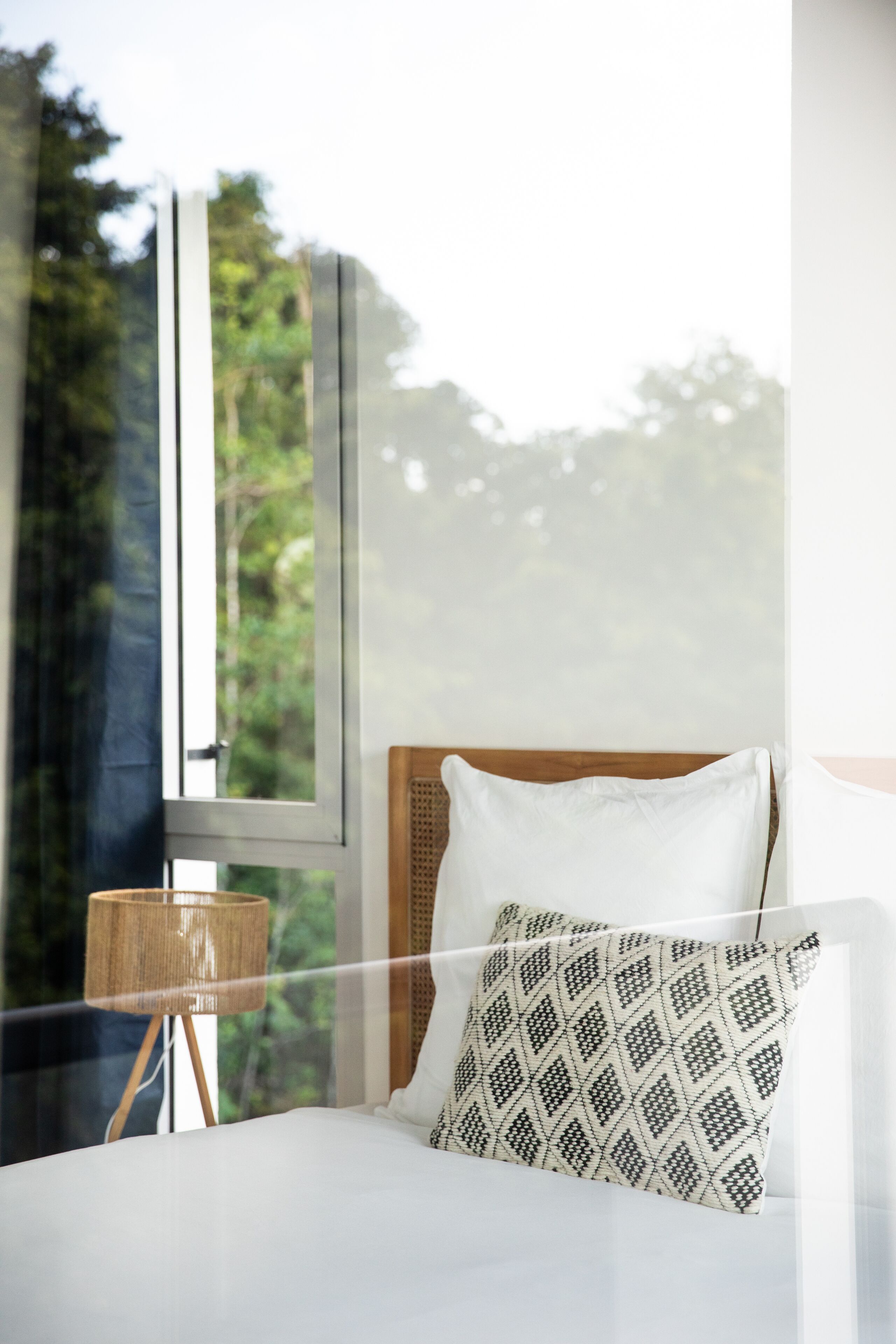 A bedroom with a large window, a bed with white bedding, a patterned pillow, and a wooden headboard.