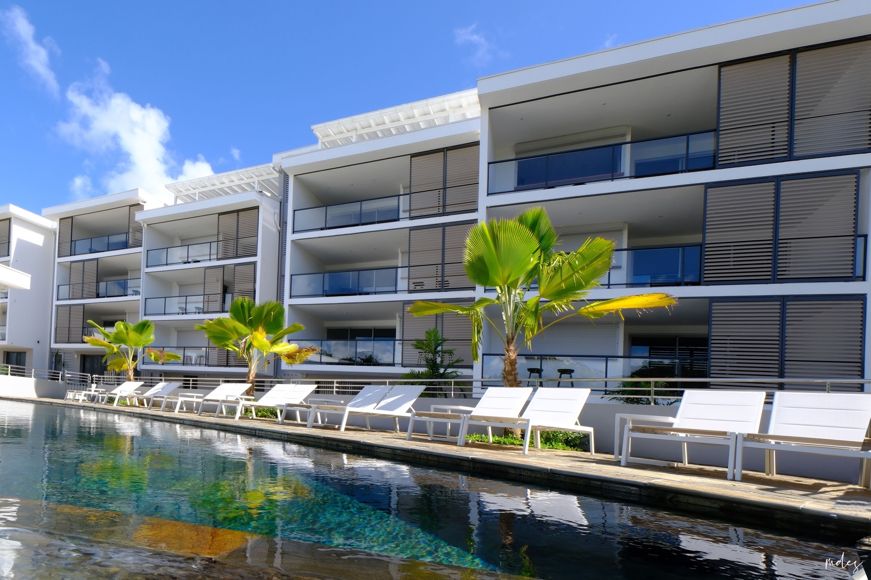 A modern hotel with multiple balconies, a swimming pool, and sun loungers.
