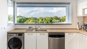 A modern kitchen with a built-in washer and dishwasher, a large window with a view of greenery, and a wooden countertop.